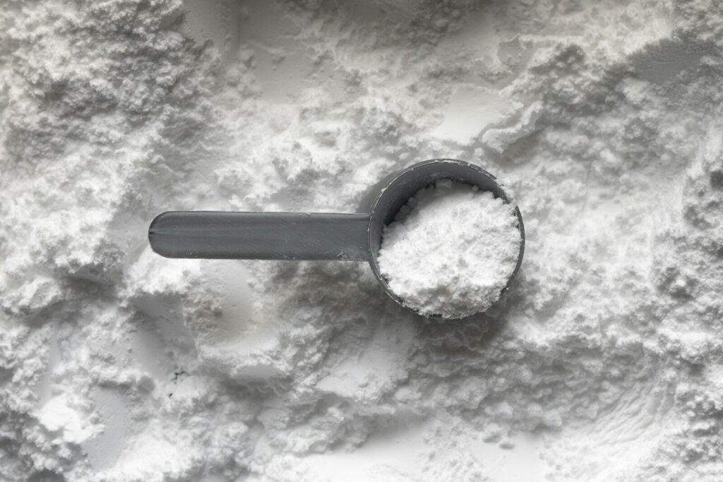 A grey plastic scoop filled with white powder resting on a pile of powder