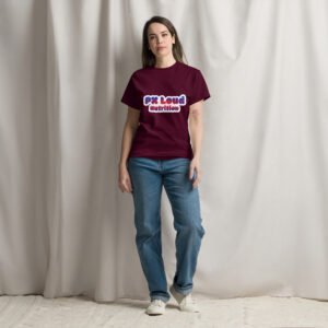 A woman stands in front of a beige curtain, wearing a maroon Unisex classic tee from PK Loud Nutrition, paired with blue jeans and white sneakers.